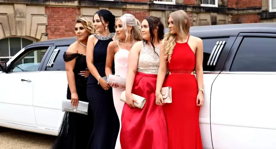 Studentesse della Scoil Ruáin sono in piedi davanti a una limousine bianca davanti a un edificio in mattoni.