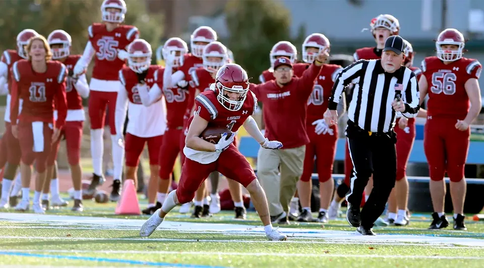 Un giocatore di football americano della Loomis Chaffee School corre con la palla sul campo accanto a un arbitro.