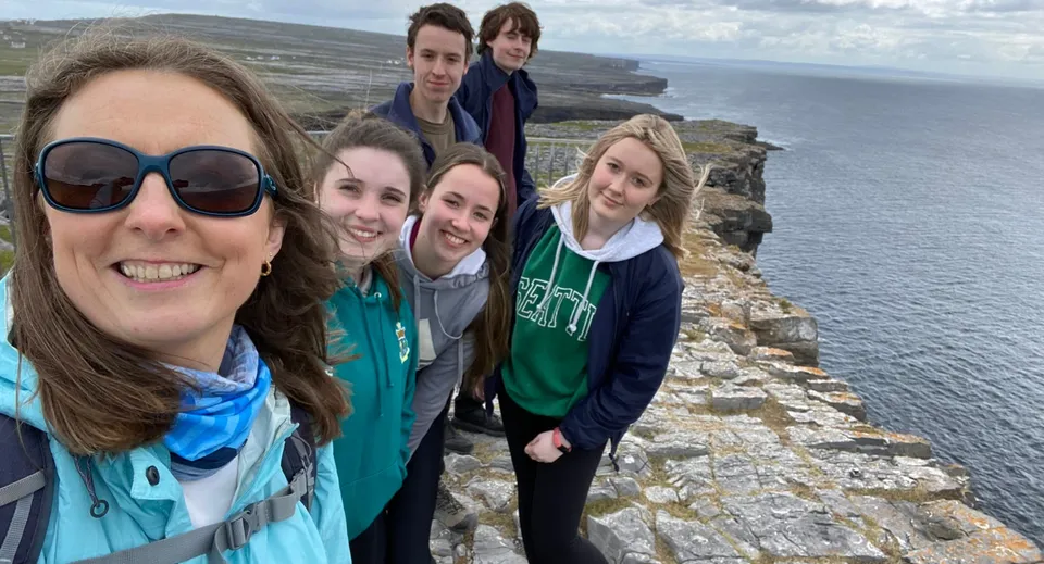 Un gruppo di studenti del Sancta Maria College si scatta un selfie davanti a un paesaggio costiero con scogliere e mare sullo sfondo.