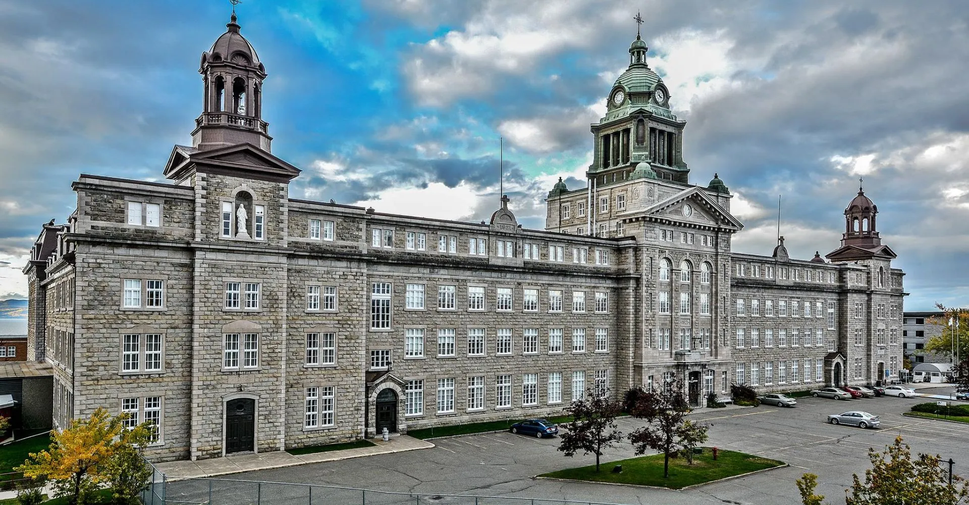 L'edificio principale storico del Collège de Sainte-Anne-de-la-Pocatière con torri e cupole circondato da un cortile interno pavimentato e alberi verdi.