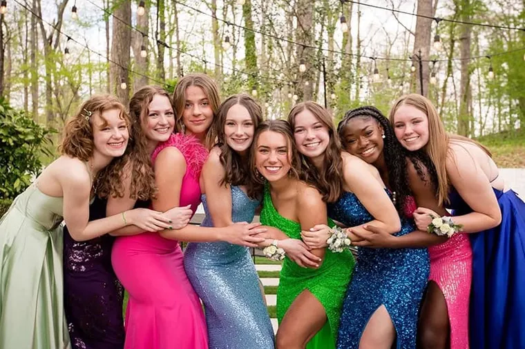 Grupo de jóvenes con vestidos elegantes de colores abrazadas y sonrientes al aire libre
