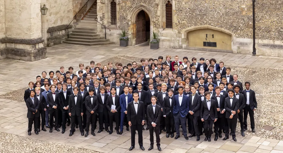 Un gruppo di studenti in abito formale è in piedi davanti allo storico edificio in pietra del Winchester College.