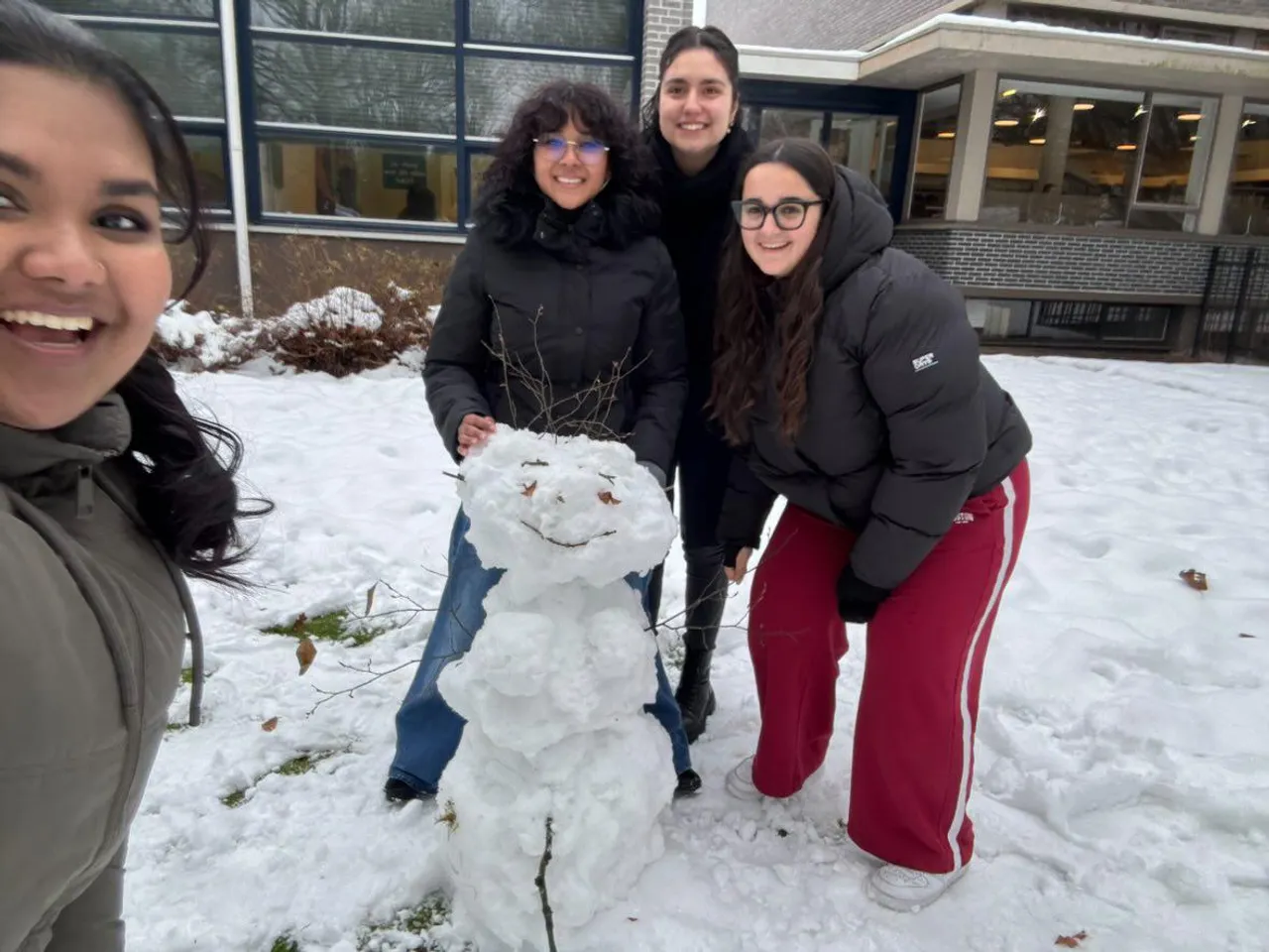 Quattro studenti sorridenti accanto a un pupazzo di neve davanti alla scuola