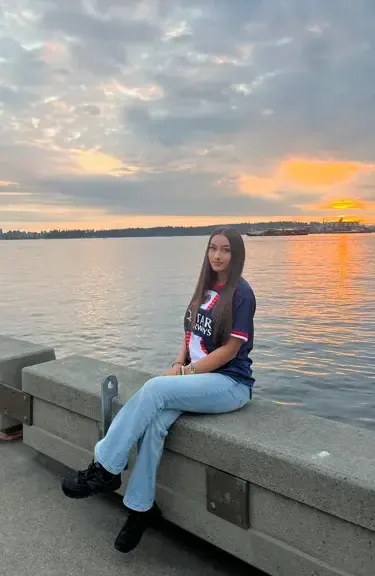 Chica sentada en un muro junto al mar durante la puesta de sol