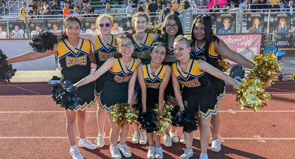Un gruppo di cheerleader in divisa gialla e nera posa sul campo sportivo della Arizona Lutheran Academy.