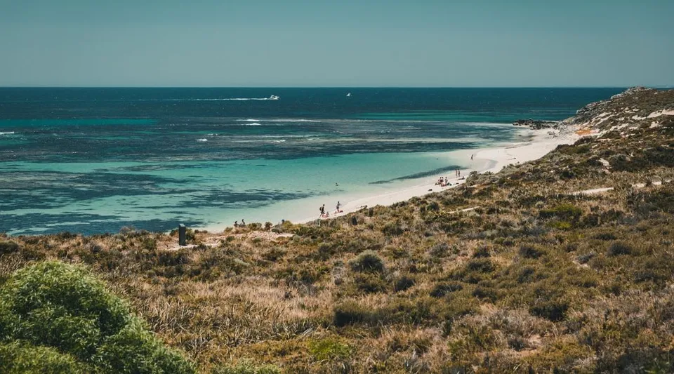Paesaggio costiero con spiaggia, acqua turchese e una collina alberata vicino alla Thornlie Senior High School.