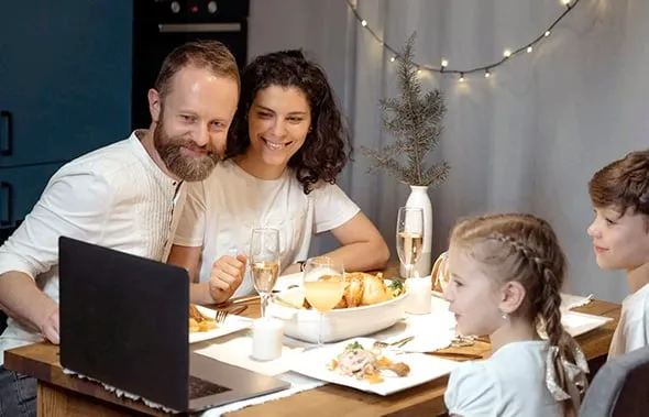 Familia reunida en la mesa hace una videollamada con el portátil durante una cena festiva