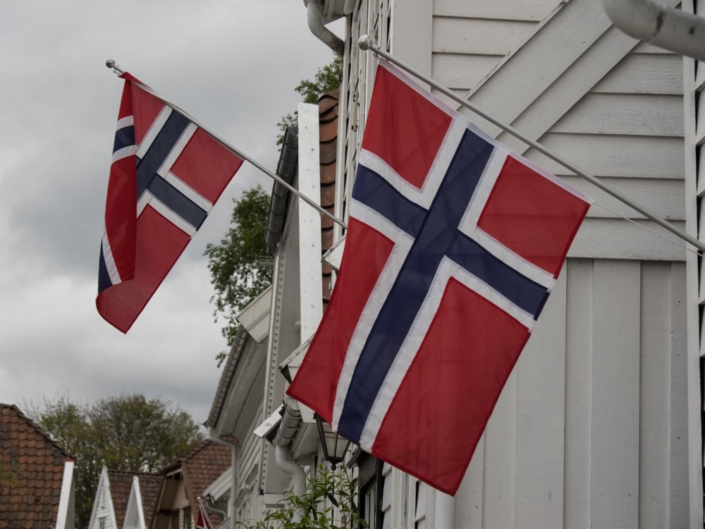 Norwegische Flaggen an weißen Holzhäusern unter bewölktem Himmel