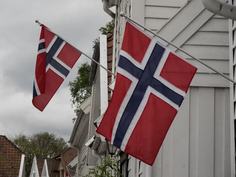 Norwegische Flaggen an weißen Holzhäusern unter bewölktem Himmel