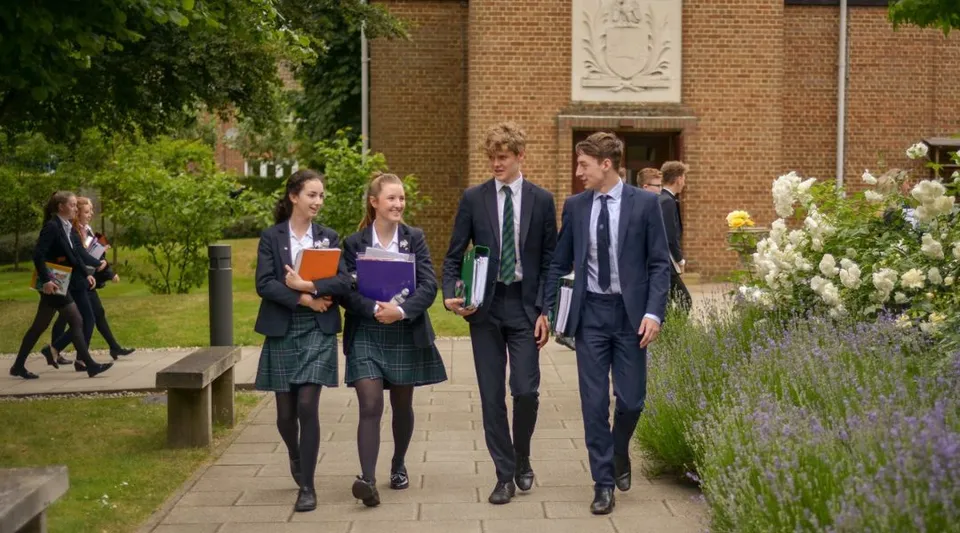 Un gruppo di studenti cammina insieme su un viale circondato dal verde davanti a un edificio in mattoni nel campus della St. John’s School a Leatherhead.