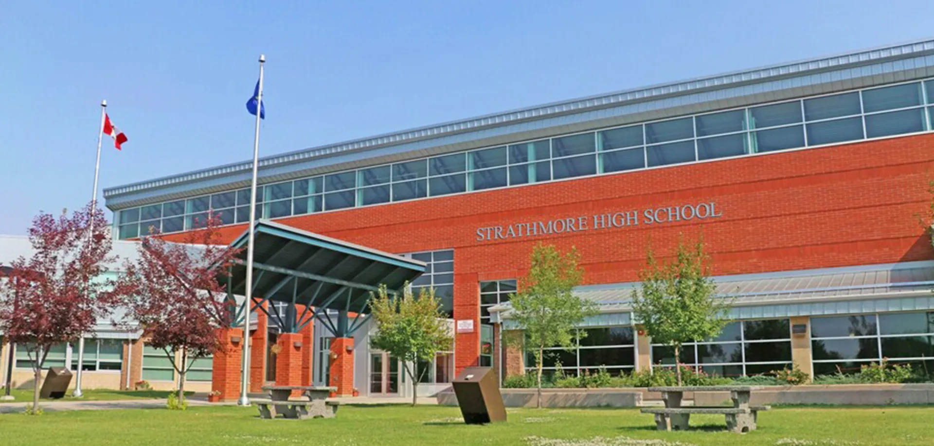 L'edificio in mattoni rossi della Strathmore High School con la scritta sulla facciata, pennoni e tavoli da picnic sul prato.