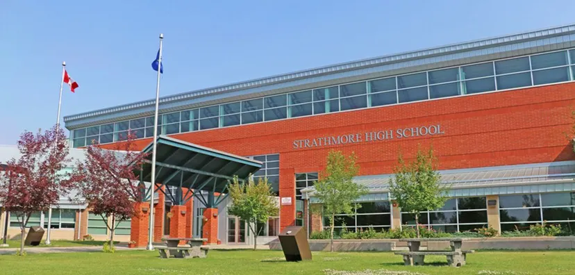 L'edificio in mattoni rossi della Strathmore High School con la scritta sulla facciata, pennoni e tavoli da picnic sul prato.