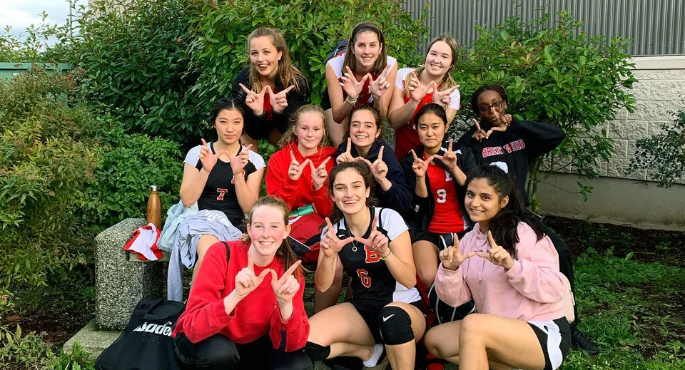 Un gruppo di studentesse della Chemainus Secondary School si trova all'aperto in abbigliamento sportivo e fa gesti con le mani davanti a uno sfondo verde.