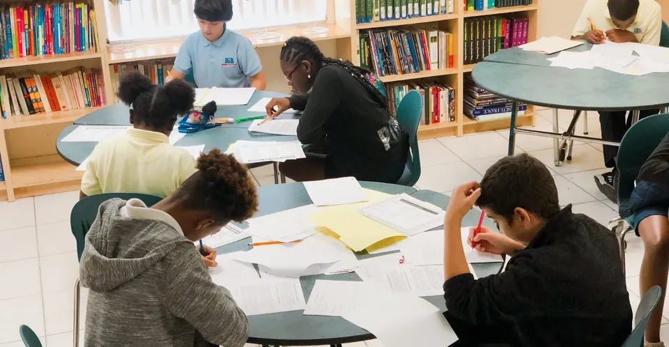 Un gruppo di studenti della International School of Broward studia insieme in biblioteca, circondato da scaffali di libri.