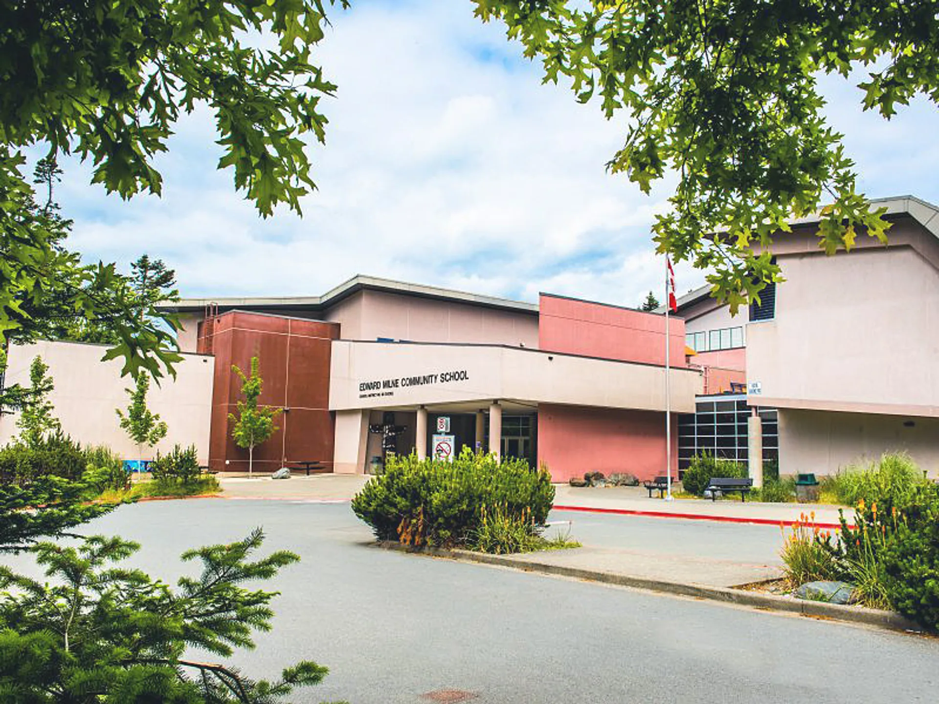 L'edificio a più piani della Edward Milne Community School con la facciata rossa è circondato da un verde rigoglioso e alberi.