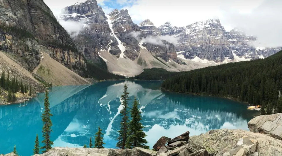 Un lago di montagna dal colore blu turchese che riflette montagne rocciose innevate e una foresta di conifere in Alberta.