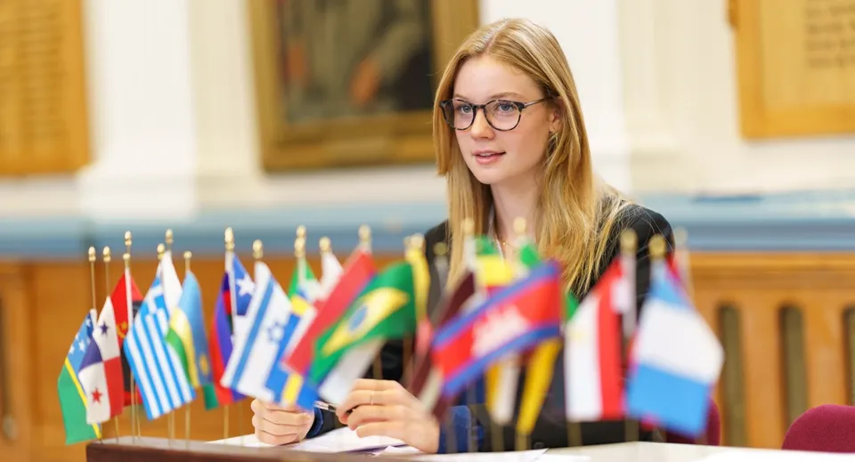 Una giovane donna con gli occhiali si trova davanti a un'esposizione di bandiere internazionali nell'area della Royal Russell School.