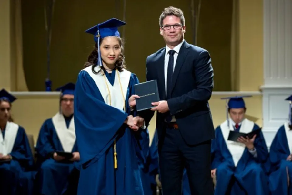 Una neodiplomata della Fredericton Christian Academy riceve il suo diploma da un uomo in abito scuro.