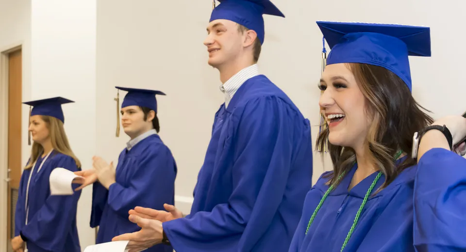 Un gruppo di diplomati della Ormeau Woods State High School si trova insieme nel corridoio in abiti blu con i cappelli.