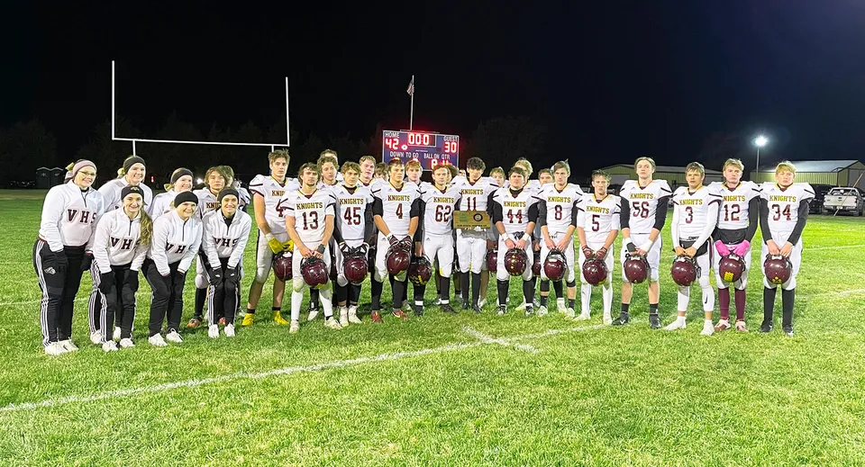 Un gruppo di studenti della Victoria High School si trova in maglia bianca sul campo da calcio di notte.