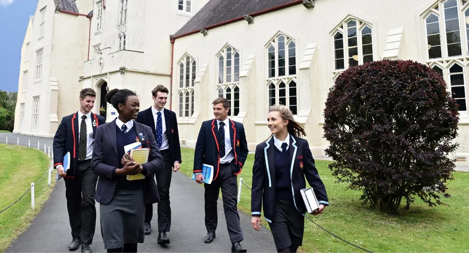 Un gruppo di studenti in divisa scolastica cammina insieme nel cortile del Llandovery College dall'architettura gotica.