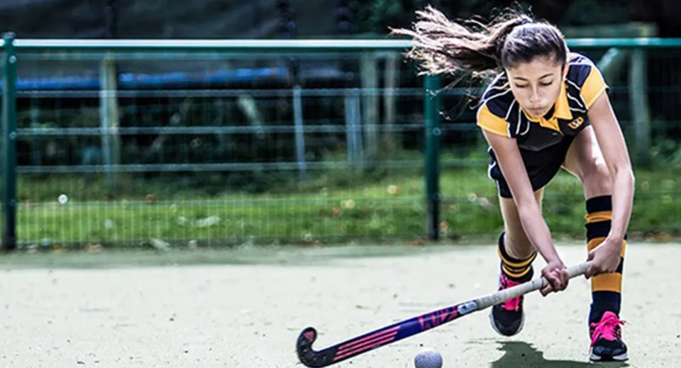 Una giovane atleta della Bedstone School si concentra sulla pallina da hockey sul campo sportivo.