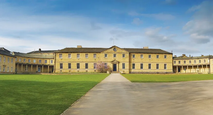 L'edificio principale giallo della Ackworth School si trova su un grande prato sotto un cielo blu con nuvole.