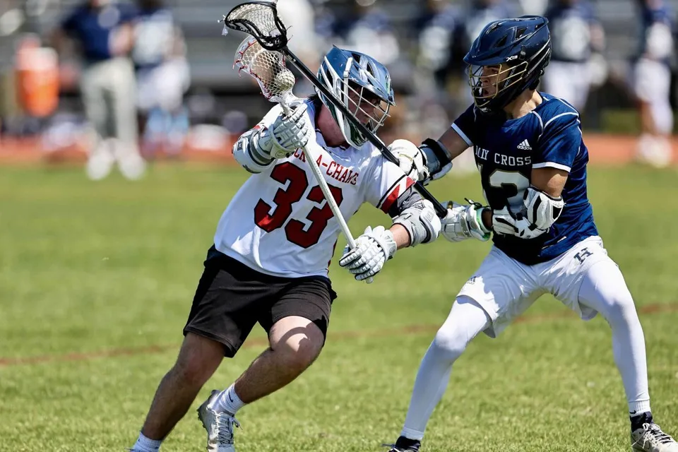 Un giocatore di lacrosse della Saint Stanislaus Catholic High School affronta un avversario su un campo in erba.