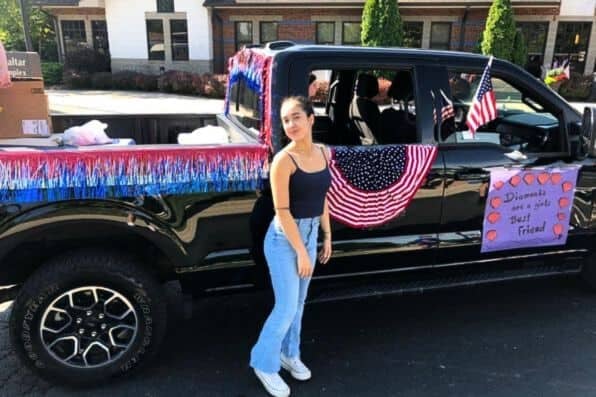 Joven junto a una camioneta negra decorada con banderas estadounidenses y adornos festivos