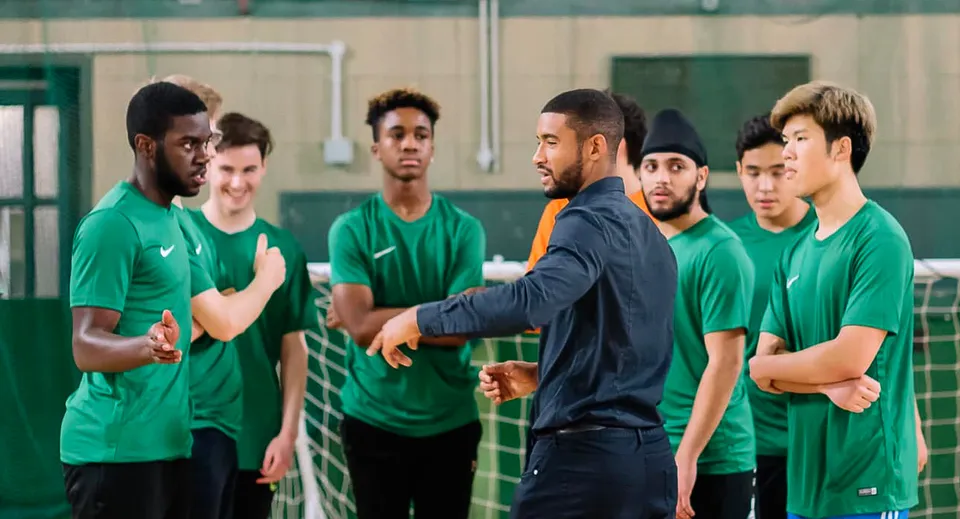 Un gruppo di studenti del David Game College discute una strategia di squadra con il proprio allenatore nel centro sportivo.