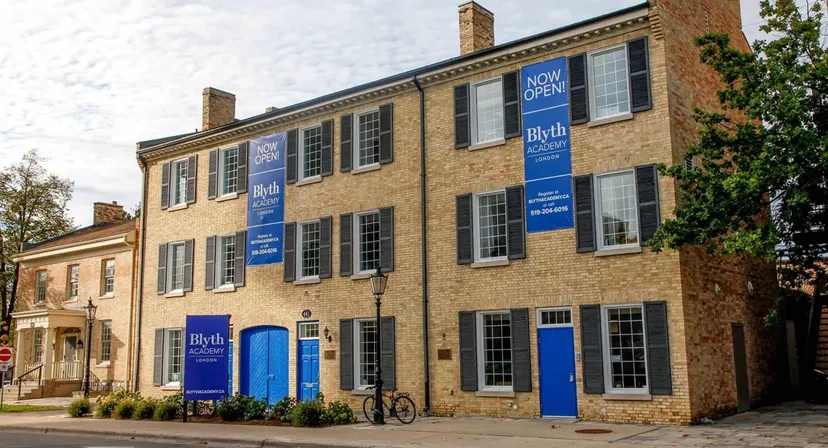 L'edificio in mattoni a più piani della Blyth Academy, con finestre e porte blu aperte, è circondato da alberi.