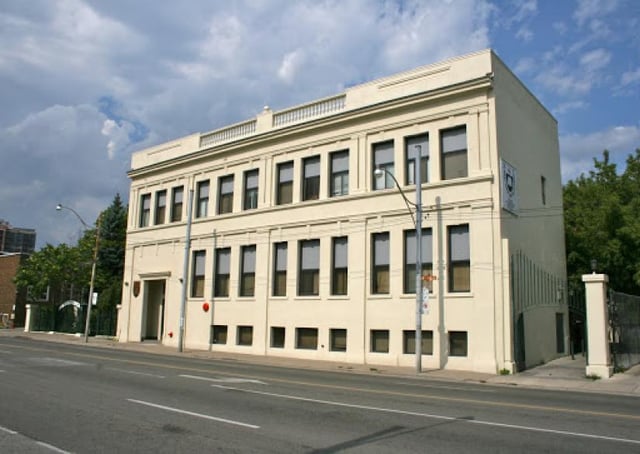 L'edificio beige a più piani del Great Lakes College of Toronto si trova su una strada alberata con un cielo nuvoloso sullo sfondo.