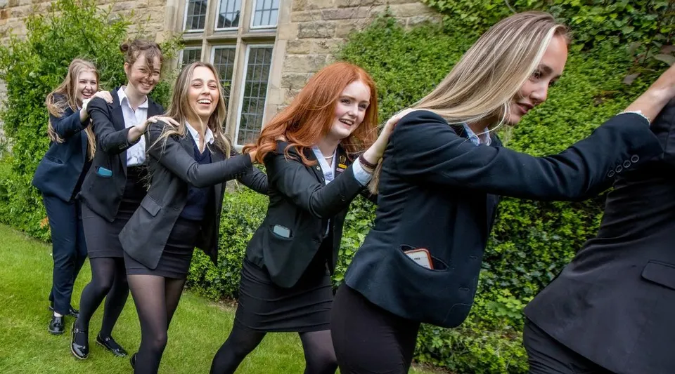 Un gruppo di giovani studentesse in completo nero sta davanti all'edificio in pietra della Rydal Penrhos School circondato da un paesaggio verde.