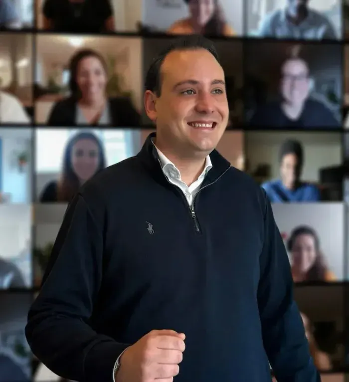 Giovane sorridente durante un webinar davanti a una parete di partecipanti in videochiamata
