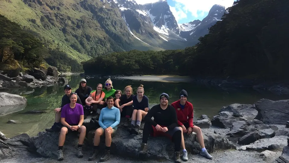 Un gruppo di studenti della Dunstan High School siede su delle rocce davanti a un lago e montagne innevate.