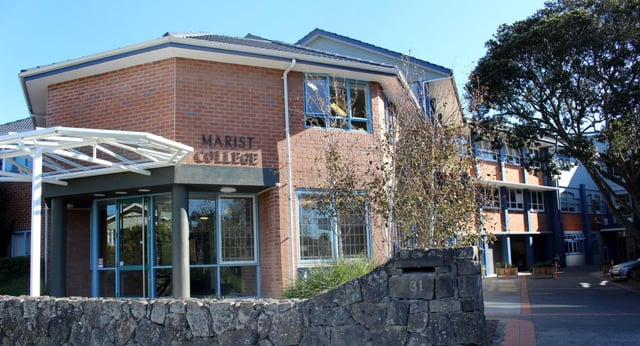 Das Backsteingebäude mit dem Schriftzug Marist College an der Fassade, umgeben von Bäumen und einer Steinmauer.