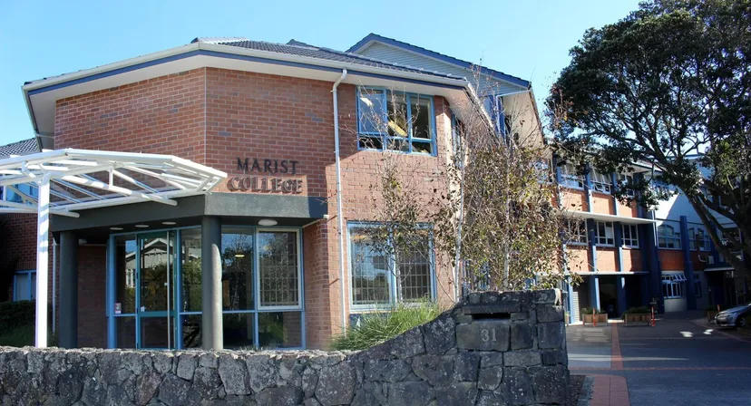 L'edificio in mattoni con la scritta Marist College sulla facciata, circondato da alberi e un muro di pietra.