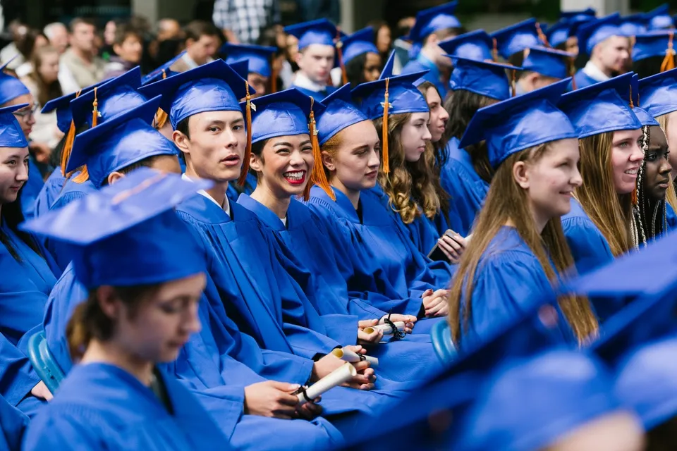 Un grande gruppo di diplomati della Jules Verne school Vancouver indossa l'abito blu della cerimonia di diploma e sta insieme.