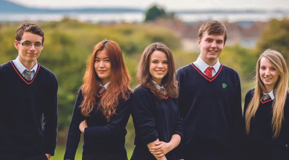 Un gruppo di cinque studenti in divisa scolastica si trova davanti a un paesaggio montano nel campus della St. Michael’s School.