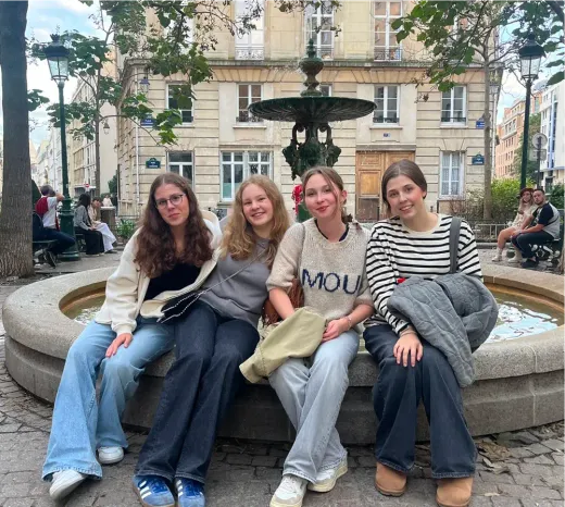 Vier Mädchen sitzen auf dem Rand eines Brunnens auf einem Platz in Frankreich