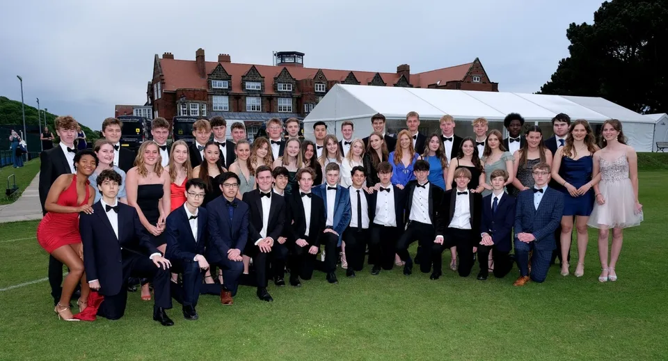 Un grande gruppo di studenti del Scarborough College si trova su un prato davanti a un edificio storico con tetti di tegole rosse.