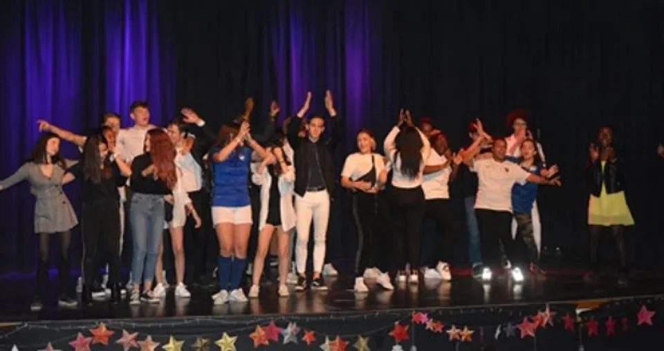 Un gruppo di studenti e studentesse sul palco del Campus La Salle Saint Christophe con le braccia alzate davanti a un sipario scuro e luci colorate.