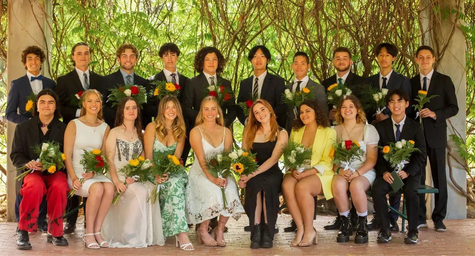 Un gruppo di studenti della Ojai Valley School in abiti eleganti posa con mazzi di fiori.