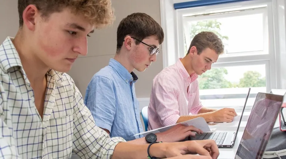 Tre studenti della Rookwood School lavorano concentrati con dei laptop in una stanza luminosa.