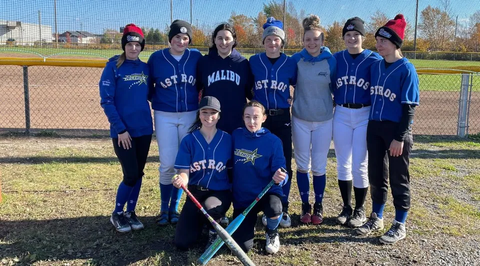 Un gruppo di giovani atlete in divisa blu si trova insieme sul campo da baseball della Ascension Collegiate.