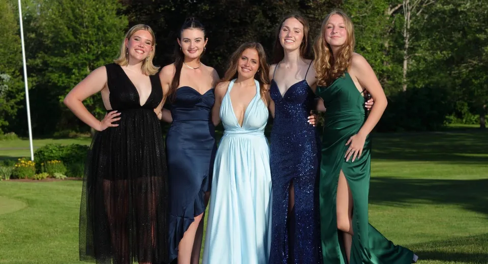 Un gruppo di cinque studentesse del John Abbott College posa in abiti da sera eleganti in uno spazio verde all'aperto.
