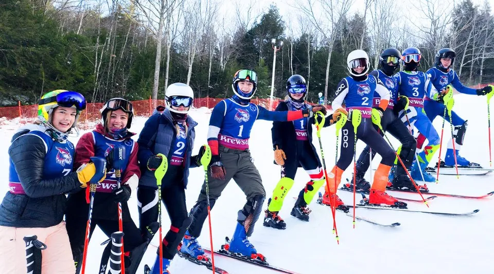 Un gruppo di sciatori in uniformi colorate si trova su un pendio innevato all'interno del campus della Brewster Academy.