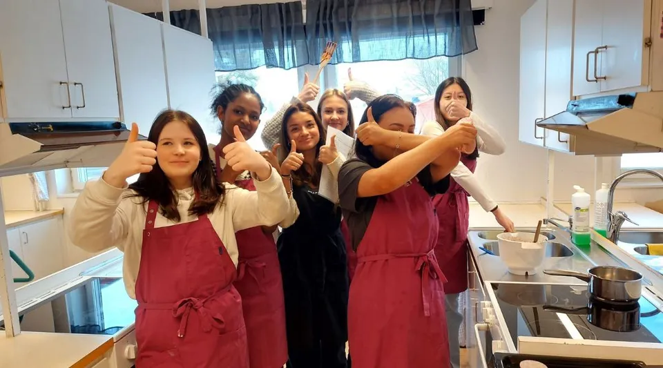 Un gruppo di giovani donne con grembiuli rossi si trova nella cucina del Carmelitas Cadiz Colegio e fa gesti con le mani.