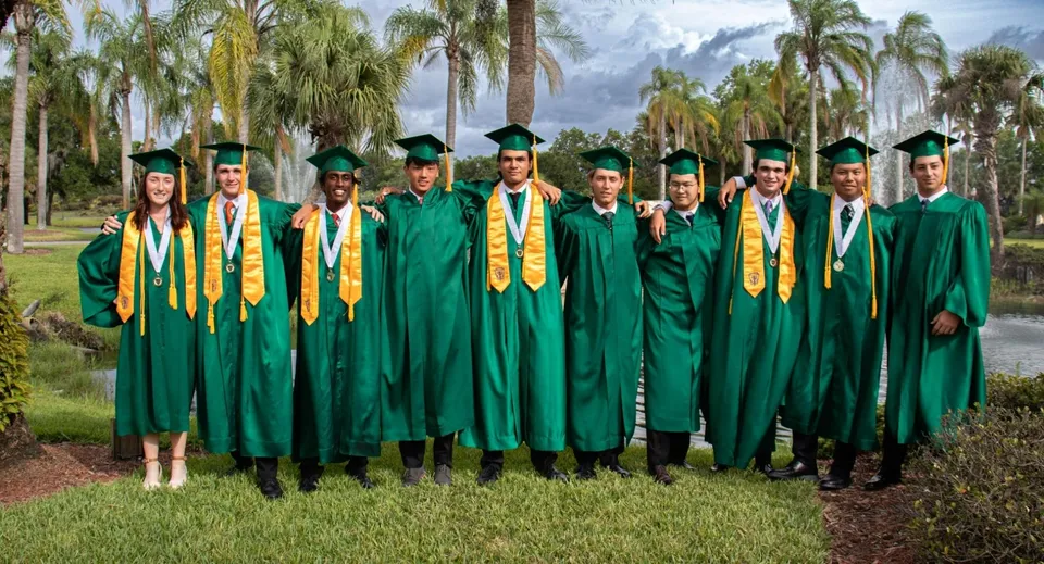 I diplomati della Saddlebrook Preparatory School in toga verde e fascia gialla si trovano all'esterno tra le palme.