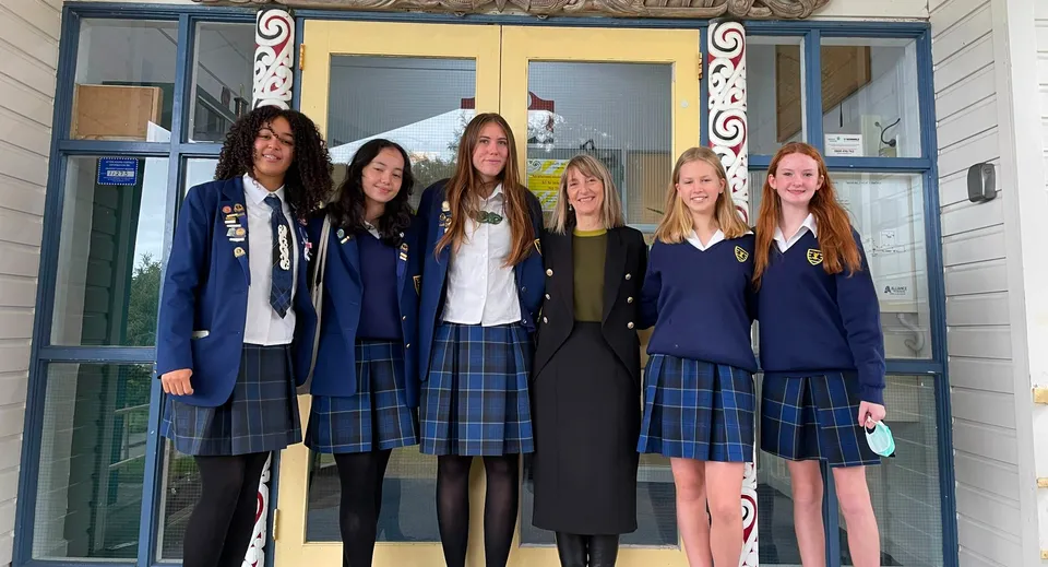 Un gruppo di sei studentesse in divisa scolastica si trova davanti a un edificio del Wellington East Girls’ College con dettagli architettonici decorati.